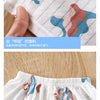 Close-up of a white cotton pajama fabric with light pastel designs and a hand touching the material.