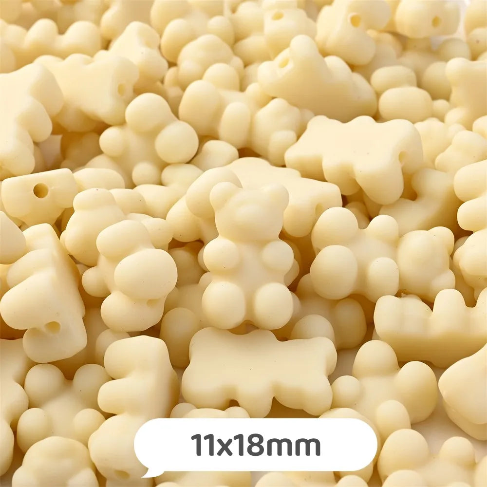 A close-up view of small, pale yellow bear-shaped acrylic craft beads scattered on a surface.