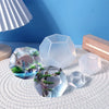 Clear geometric resin casting molds of various shapes resting on a white textured surface.