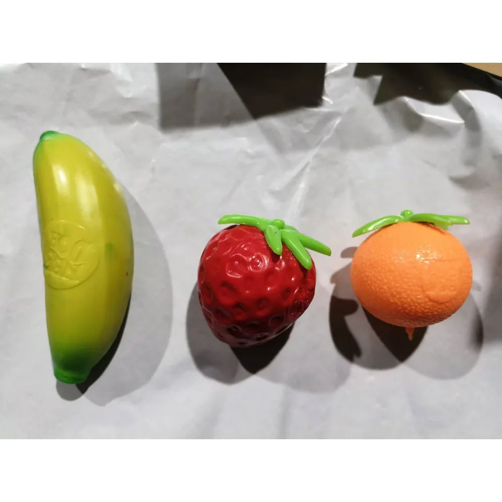 A set of three squishy fidget toys: a green banana, a red strawberry, and an orange fruit.