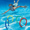 A smiling girl is jumping in clear blue water with a set of colorful pool diving rings.