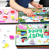 A toddler is interacting with an interactive learning book featuring insects and colorful stickers.