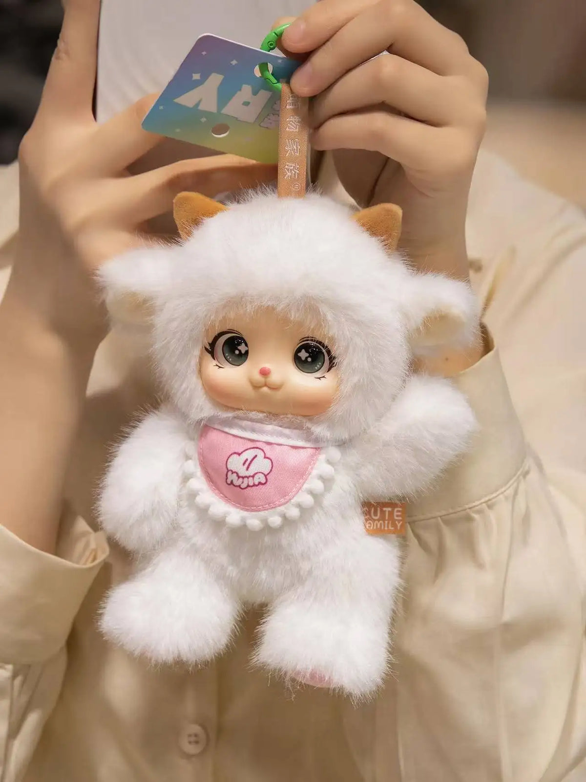 A fluffy white plush pendant featuring a cute animal face design, held by a person.