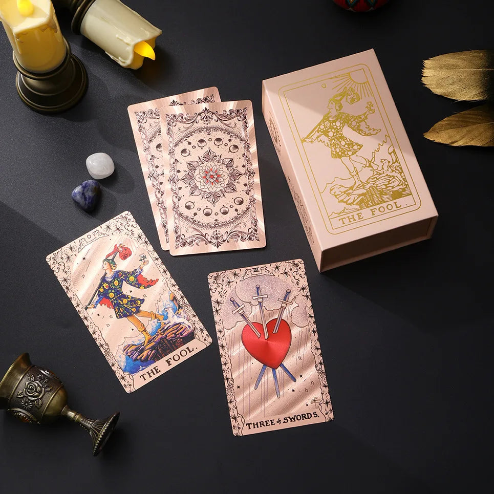 A set of gold foil tarot cards featuring a rose pink oracle finish and illustrations, displayed on a dark surface.