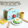 A light blue make-house bread machine toy with a wooden food item and play tools on a white surface.