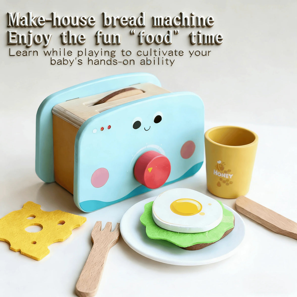 A light blue make-house bread machine toy with a wooden food item and play tools on a white surface.