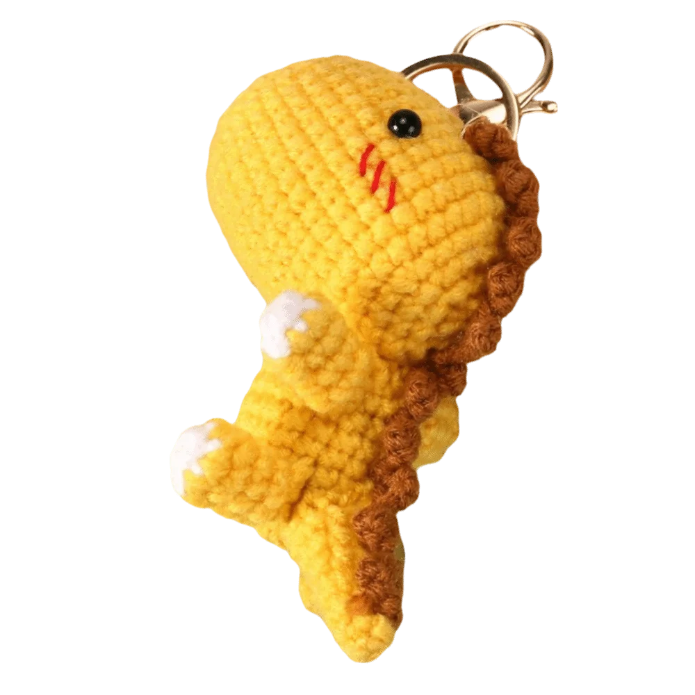 Handmade crochet yellow dinosaur keychain with brown texture and a gold ring.