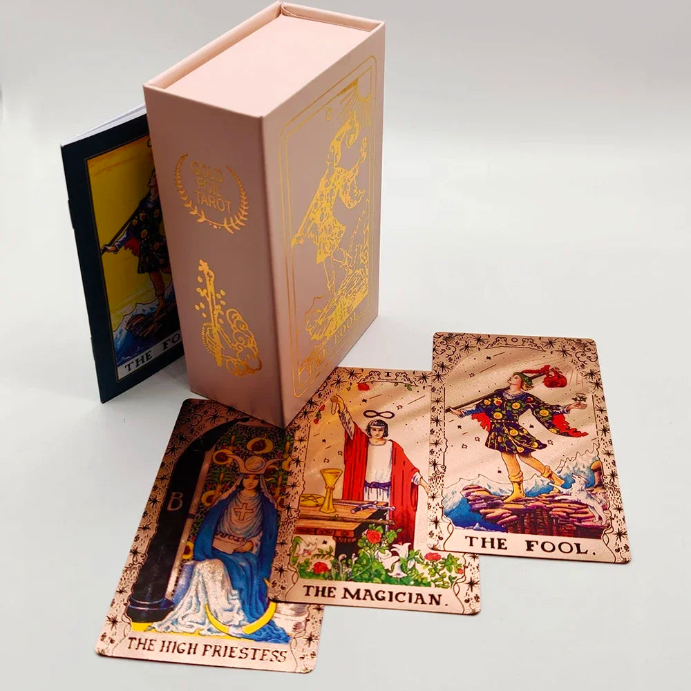 A box of gold foil tarot cards with a rose pink oracle finish and several individual cards displayed on a white surface.