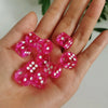 A hand holds a set of pink and clear transparent dice with white polka dots.