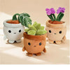Three adorable plush toys in terracotta pots with green and purple succulents.