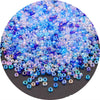 A close-up view of a pile of iridescent blue and purple glass rice beads for crafting.