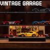 A detailed model of a vintage garage featuring various die-cast cars and a yellow sports car display.