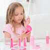 A young girl is holding a pink kids pretend makeup kit with various cosmetic items on a white table.