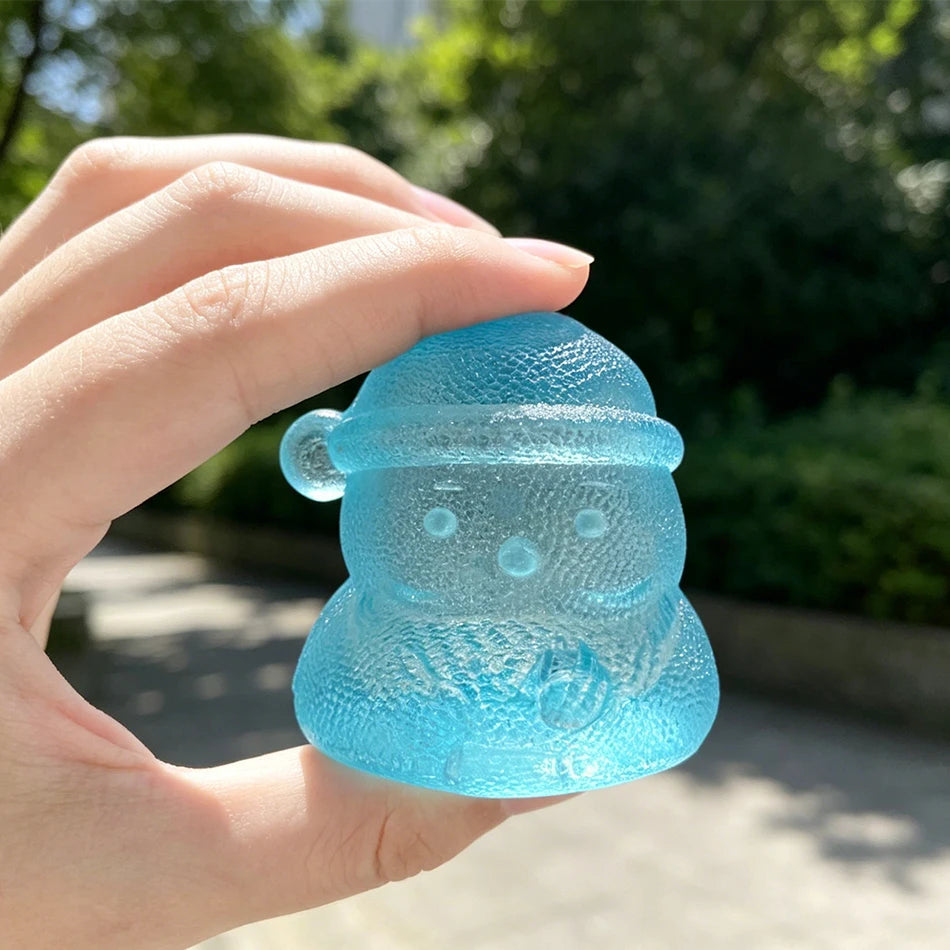 A hand holds a translucent blue holiday Santa squishy stress relief toy against a blurred green outdoor background.