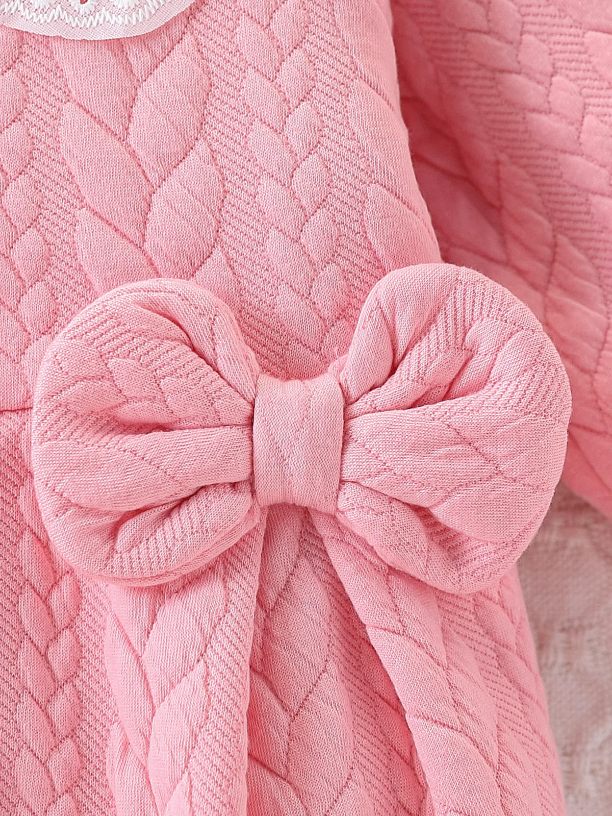 Pink quilted baby girl romper featuring a bow detail and lace collar.