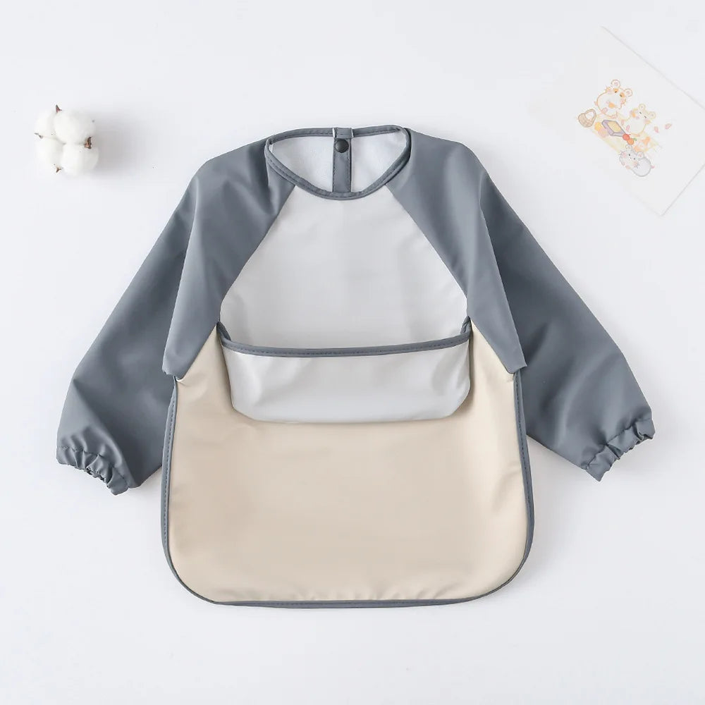 A gray and cream waterproof long-sleeved baby bib with a bib pocket shown flat on a white surface.
