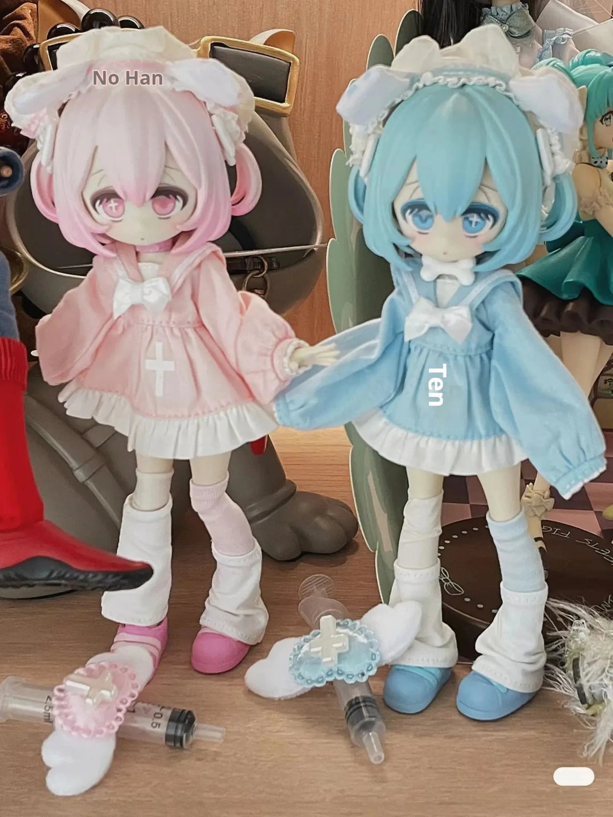 Two chibi-style vinyl art figures, one pink and one blue, are displayed next to some medical-themed items.