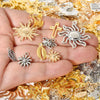 A hand holds various mixed metal charms including suns, crosses, and floral shapes for DIY jewelry making