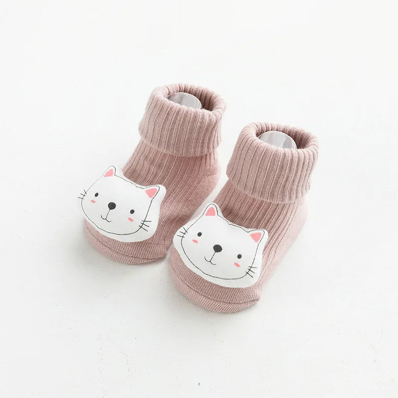 A pair of pink knitted socks featuring a white cat face design for babies and toddlers.