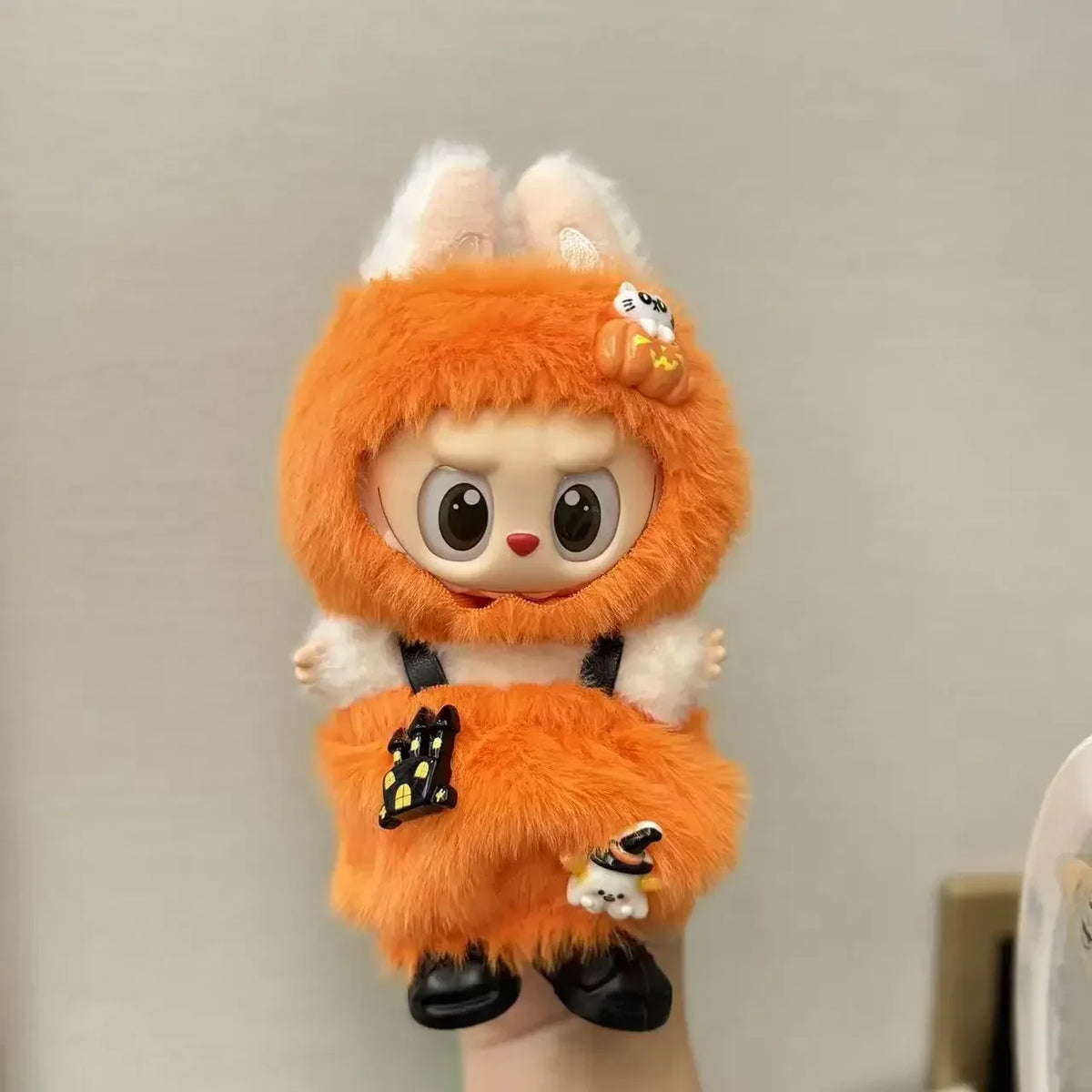 A small doll dressed in an orange pumpkin costume with white fur and black accents.