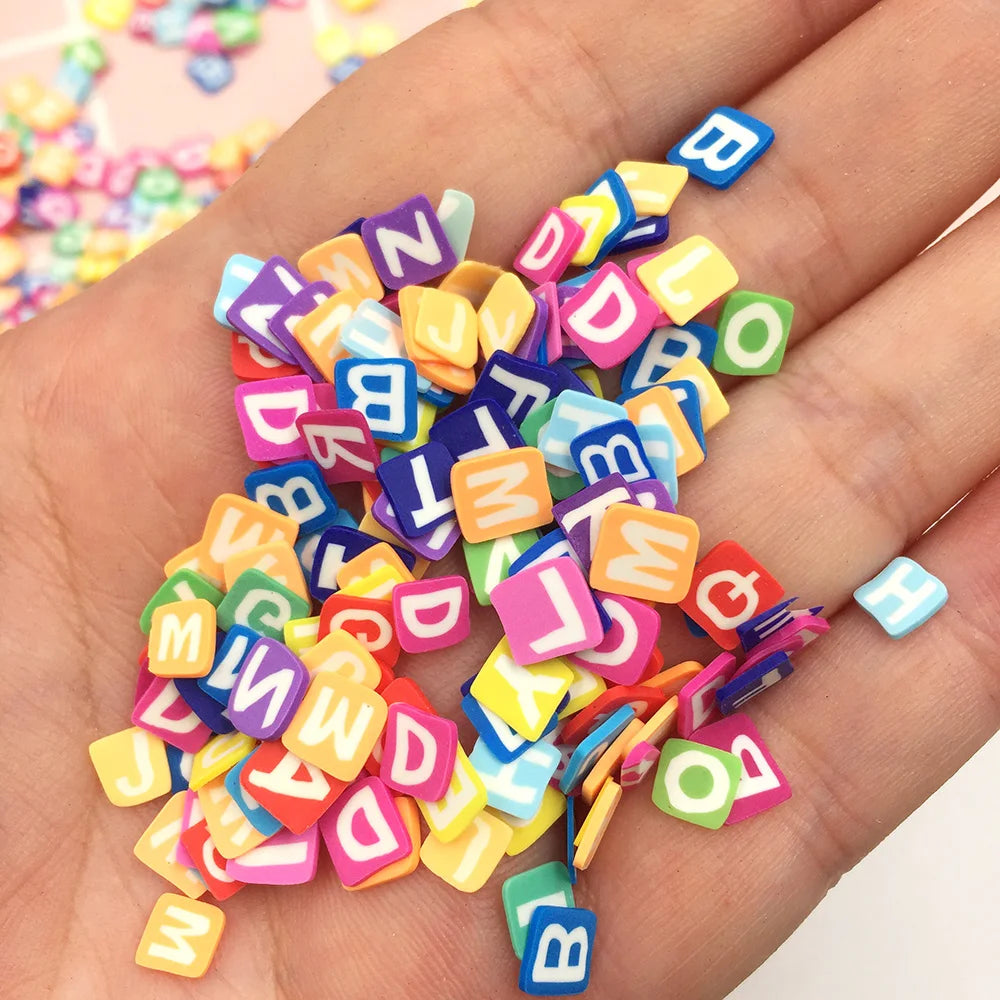 A hand holds a pile of colorful polymer clay letter sprinkles for crafts and DIY projects.