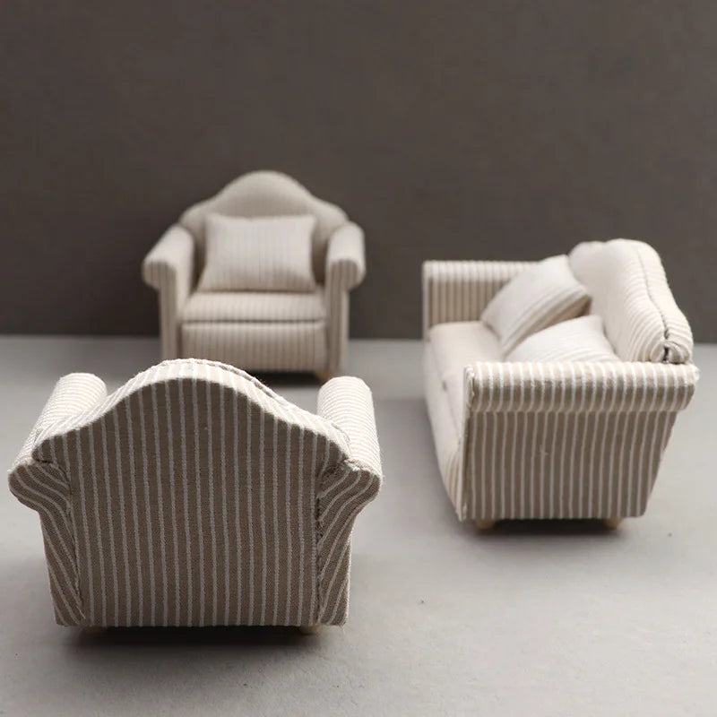 A miniature beige striped sofa and pillow set for a dollhouse display.