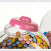 A clear dispenser filled with colorful gumballs and candies, featuring a pink lid.