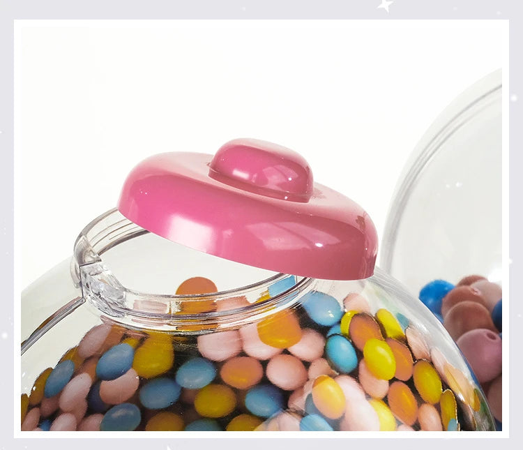 A clear dispenser filled with colorful gumballs and candies, featuring a pink lid.