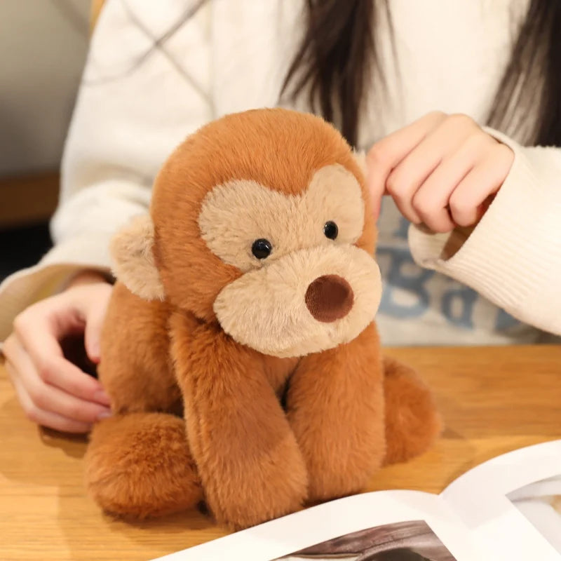 A fluffy brown plush monkey soft toy being held by a person on a wooden surface.