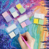 A collection of diamond painting putty wax in various pastel colors is arranged on a colorful, glittery surface.