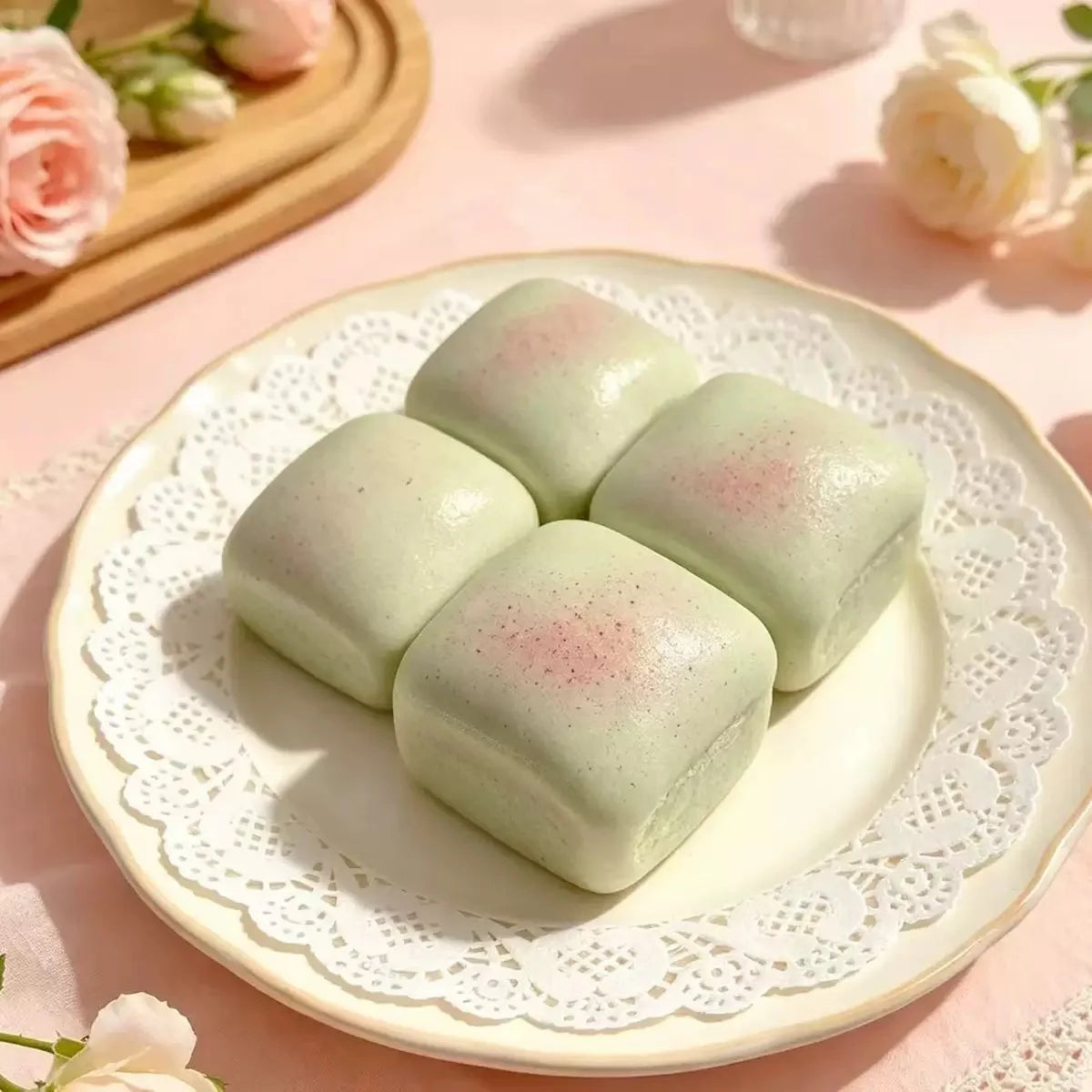 Four pale green squishy cubes arranged on a white lace plate with soft pink floral elements in the background.