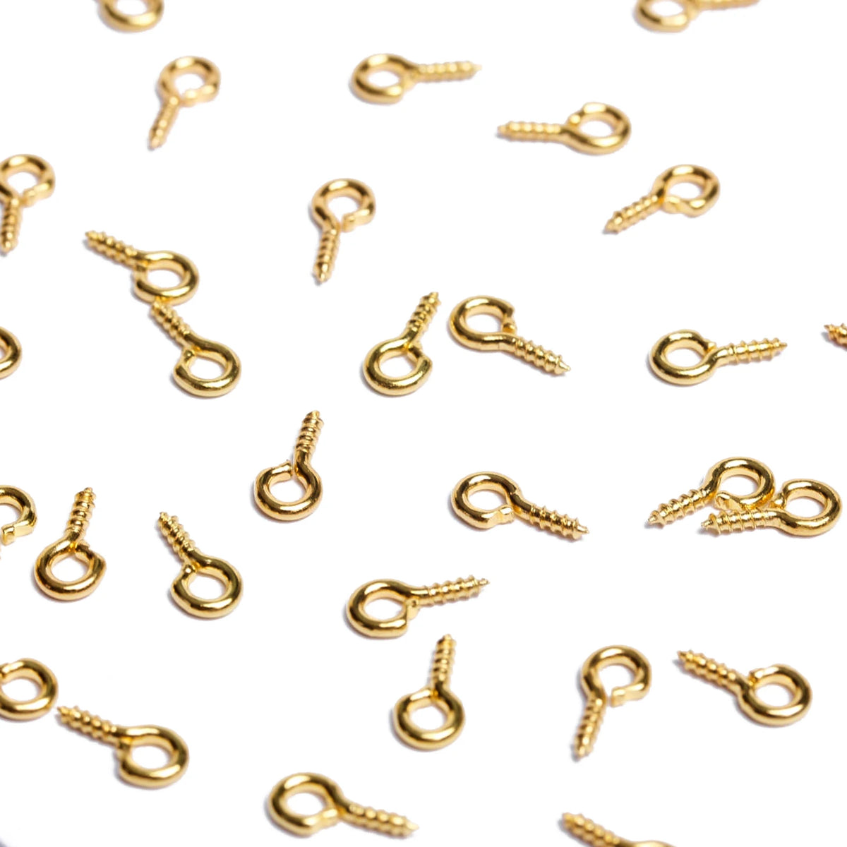 A scattered collection of gold-colored metal eye pins used for jewelry making and DIY crafts.