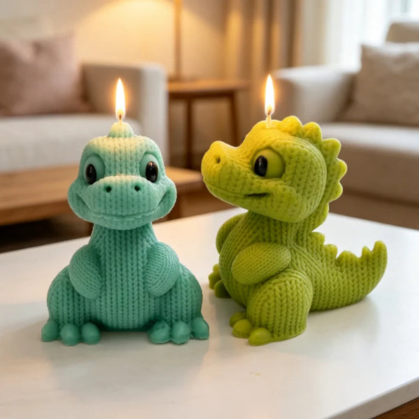 A pair of light green knitted dinosaur silicone candle molds sitting on a white surface with lit candles in the background.