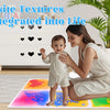A mother is playing with a baby on a colorful liquid sensory play mat in a bright room.