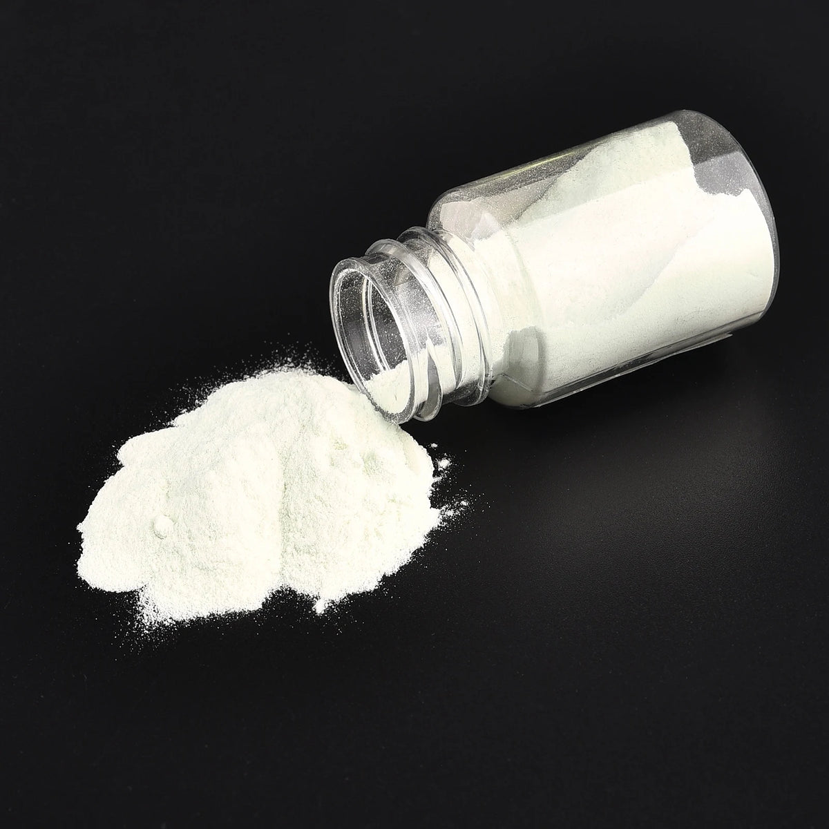 White luminous glow-in-the-dark pigment powder in a glass jar with loose powder spilled beside it