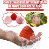 A hand is washing a red strawberry squishy fidget toy under running water.