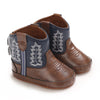 A pair of brown baby western booties with navy blue fabric detailing and a soft non-slip sole.