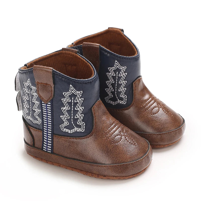 A pair of brown baby western booties with navy blue fabric detailing and a soft non-slip sole.