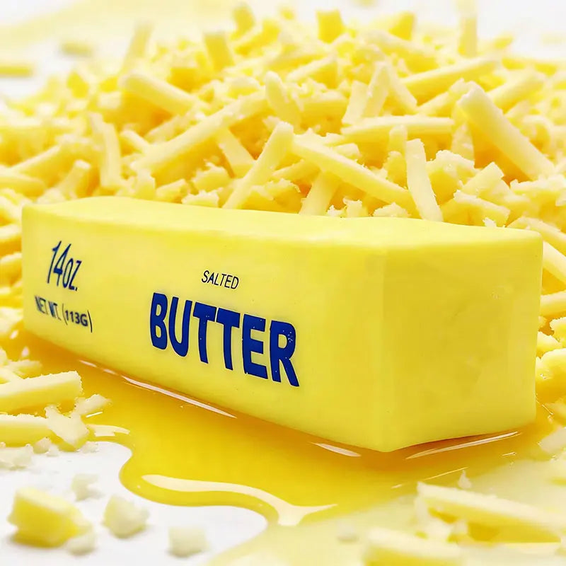 A yellow butter stick is shown with cheese shreds and melted butter dripping around it.