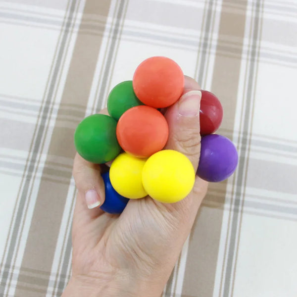 A hand is holding a collection of brightly colored stress relief balls including orange, green, red, yellow, and purple.