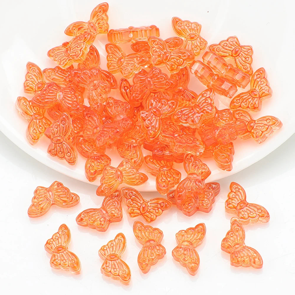 A pile of small, translucent orange glass butterfly beads for jewelry making.