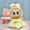 A cute, light yellow doll wearing a matching outfit and bow, sitting next to a pink chair.