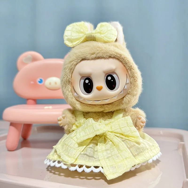 A cute, light yellow doll wearing a matching outfit and bow, sitting next to a pink chair.