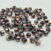 A pile of small, faceted bicone crystal glass beads in a bronze or rose gold color.