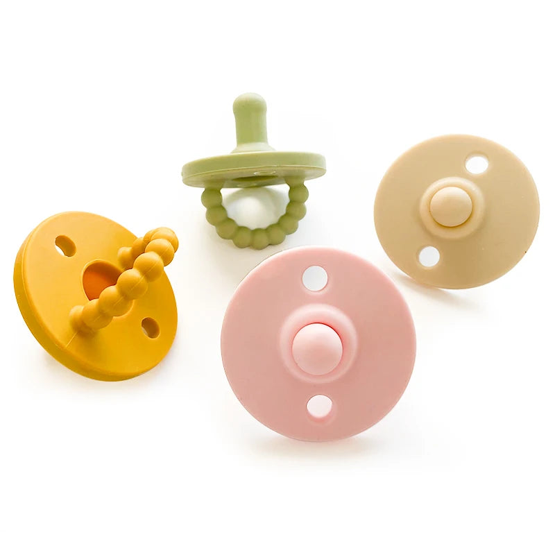 Tres chupetes o supedores de silicona para bebé en tonos amarillo, verde y rosa.
