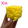 A hand holds a bright yellow, cube-shaped cheese ball stress relief squeeze toy.