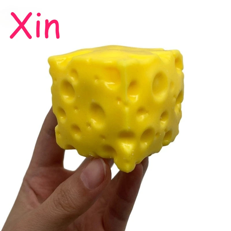 A hand holds a bright yellow, cube-shaped cheese ball stress relief squeeze toy.