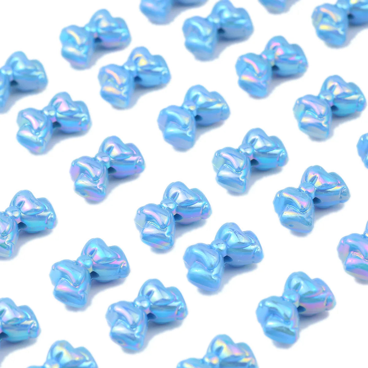A scattering of iridescent blue acrylic bow beads for jewelry making.