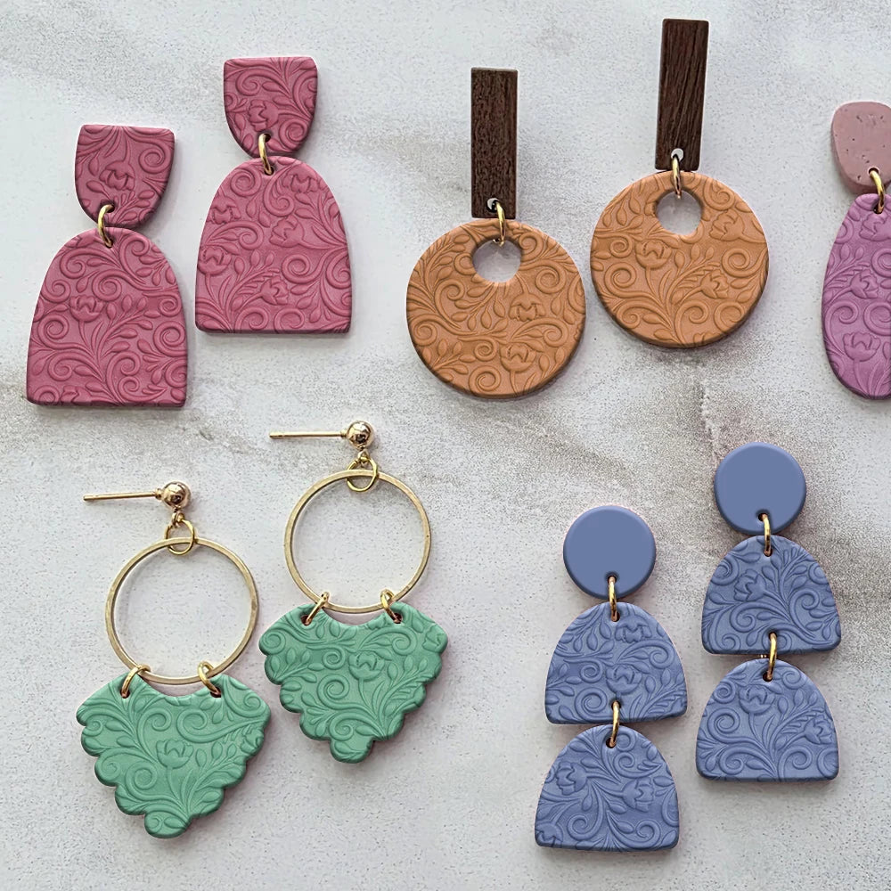 A collection of polymer clay earrings featuring various floral texture roller designs in pink, terracotta, and blue shades.
