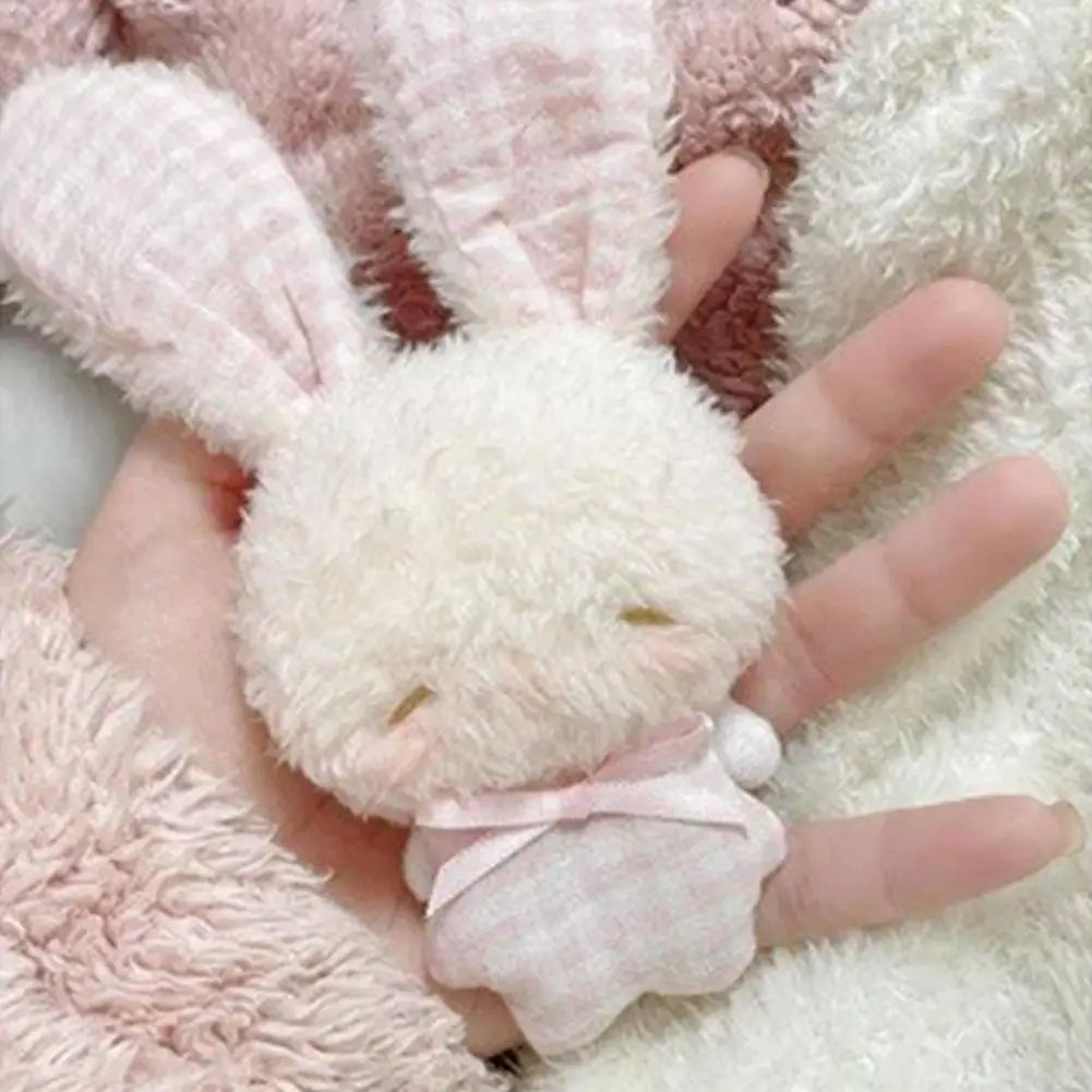 A hand is holding a fluffy white plush bunny with pink movable ears against a soft pink and white fuzzy background.